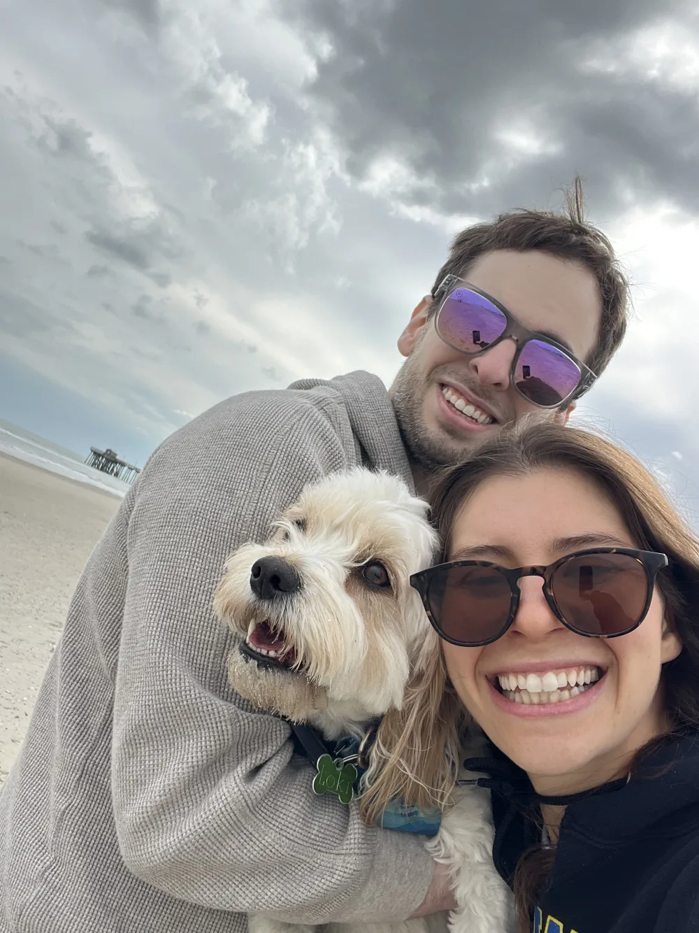 Leah and Justin in sunglasses taking a beach selfie with Loki.