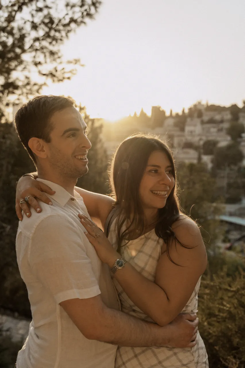 Leah and Justin embracing at golden hour on a Jerusalem hillside, the sun setting over the city behind them.