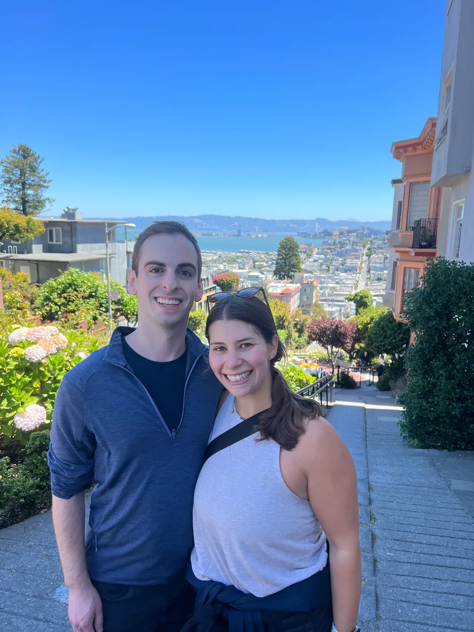 Leah and Justin at the top of Lombard Street, San Francisco and the bay behind them.
