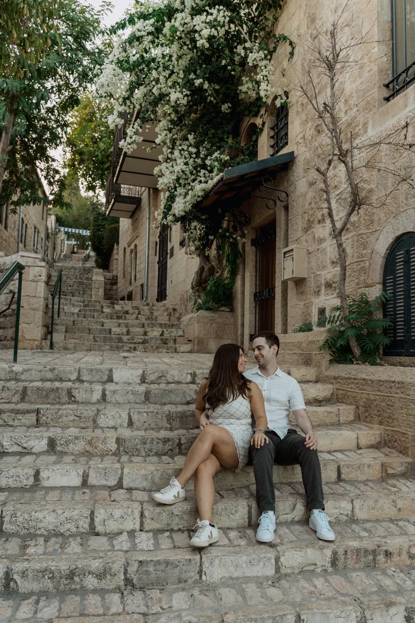 Leah and Justin smiling at each other on the flower-draped stone steps of Yemin Moshe, Jerusalem.