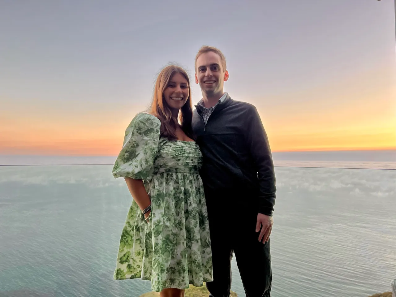 Leah and Justin dressed for dinner on a Big Sur cliffside at sunset, fog rolling over the Pacific below.