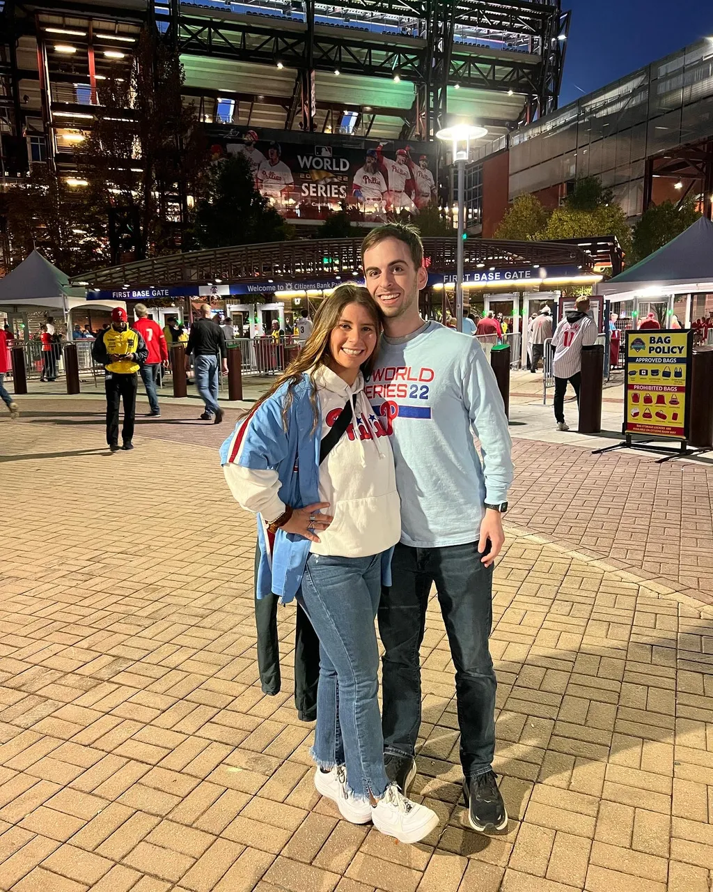 Leah and Justin in Phillies gear outside Citizens Bank Park's First Base Gate, the World Series banner glowing behind them.