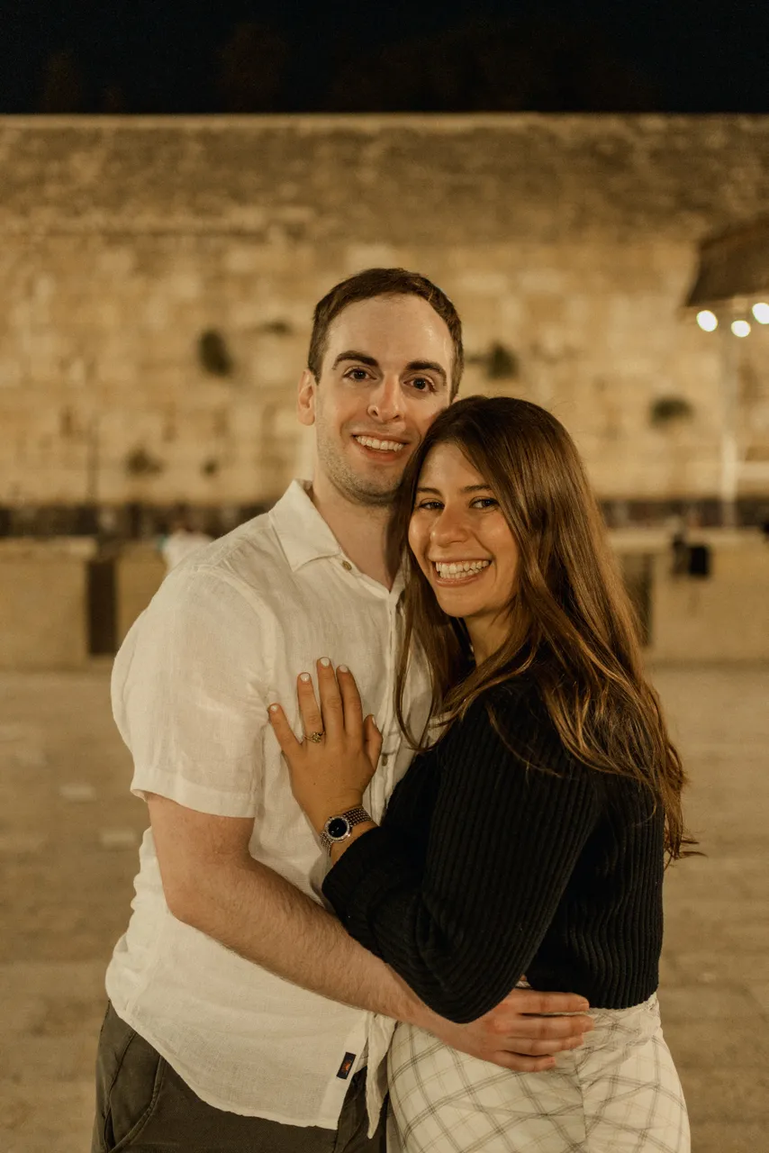 Leah and Justin embracing at night in front of the illuminated Western Wall.
